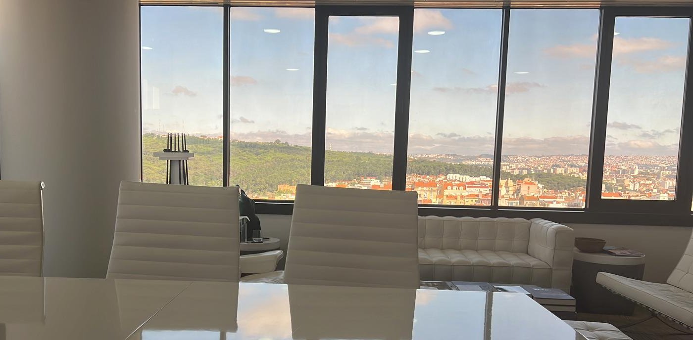 Sala de reuniões da Sustainable Goals, com mesa branca e vista panorâmica sobre Lisboa e Monsanto